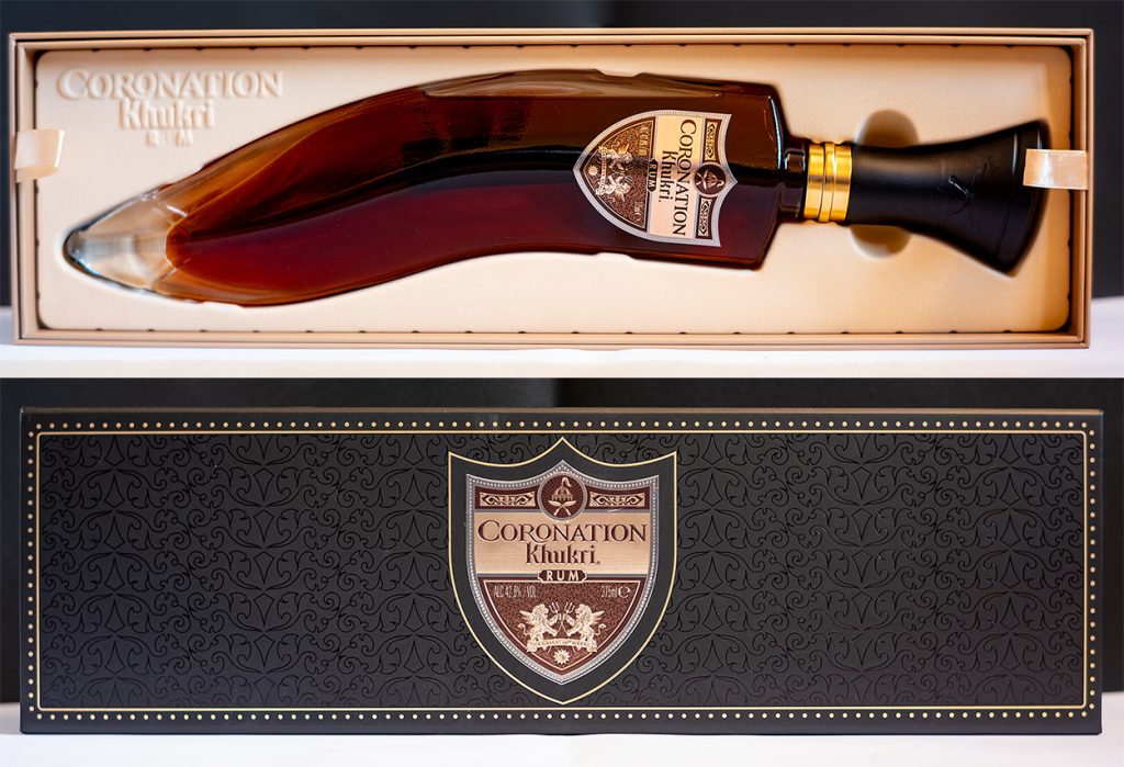 : A premium gift box of Khukri Coronation Rum featuring the dagger-shaped glass bottle and its decorative black and gold outer packaging.
